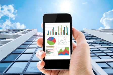 hand holding mobile phone with analyzing graph against office buildings with sun