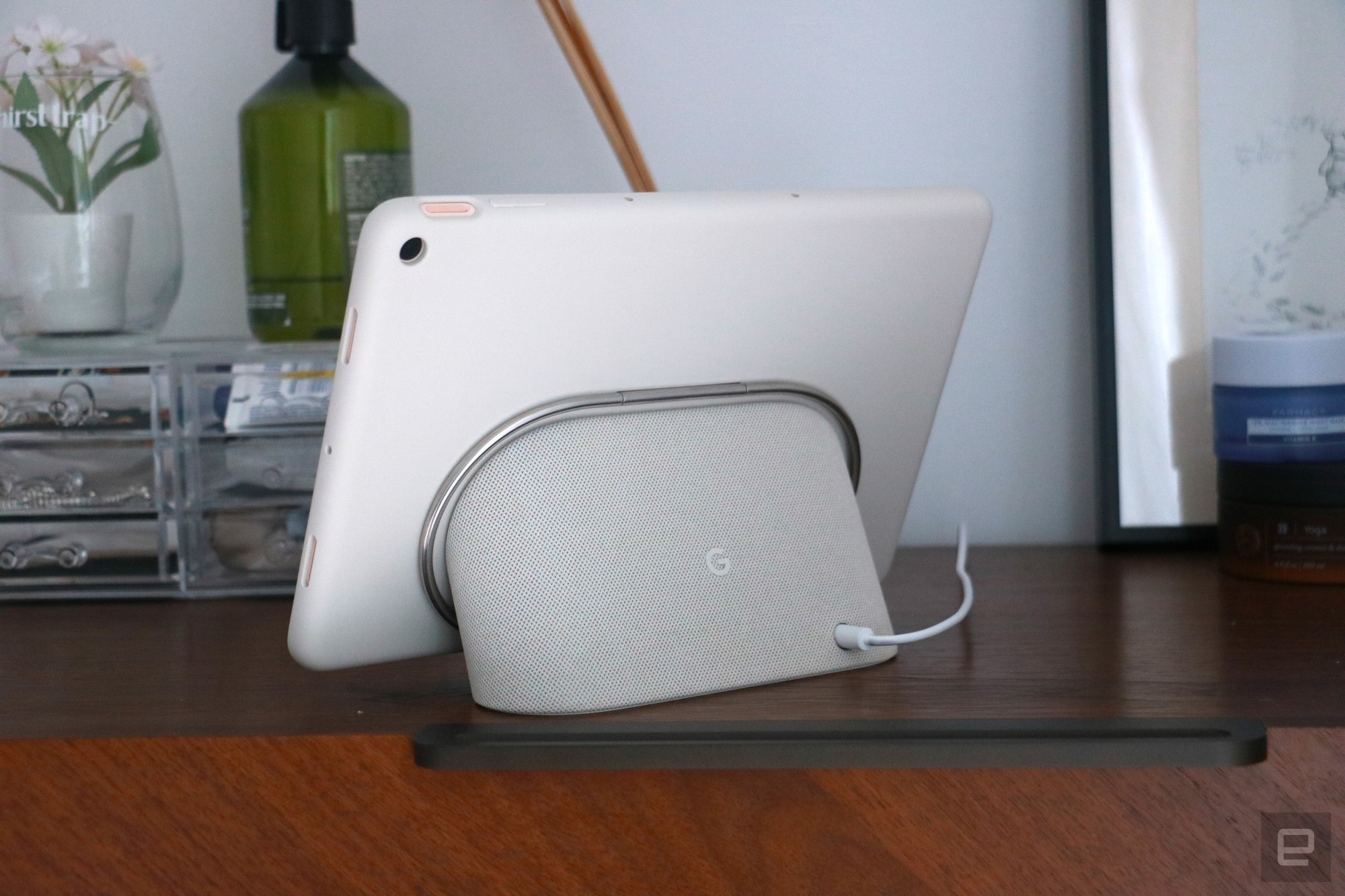 The Pixel Tablet with its protective case on and docked on the speaker base. Its silver kickstand, which is folded in, is a ring that circles the speaker. | DeviceDaily.com
