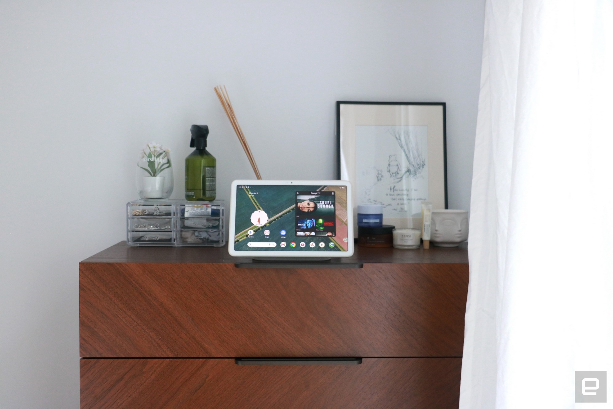 The Pixel Tablet on a walnut dresser, with various items behind it. The top two drawers are in view. | DeviceDaily.com