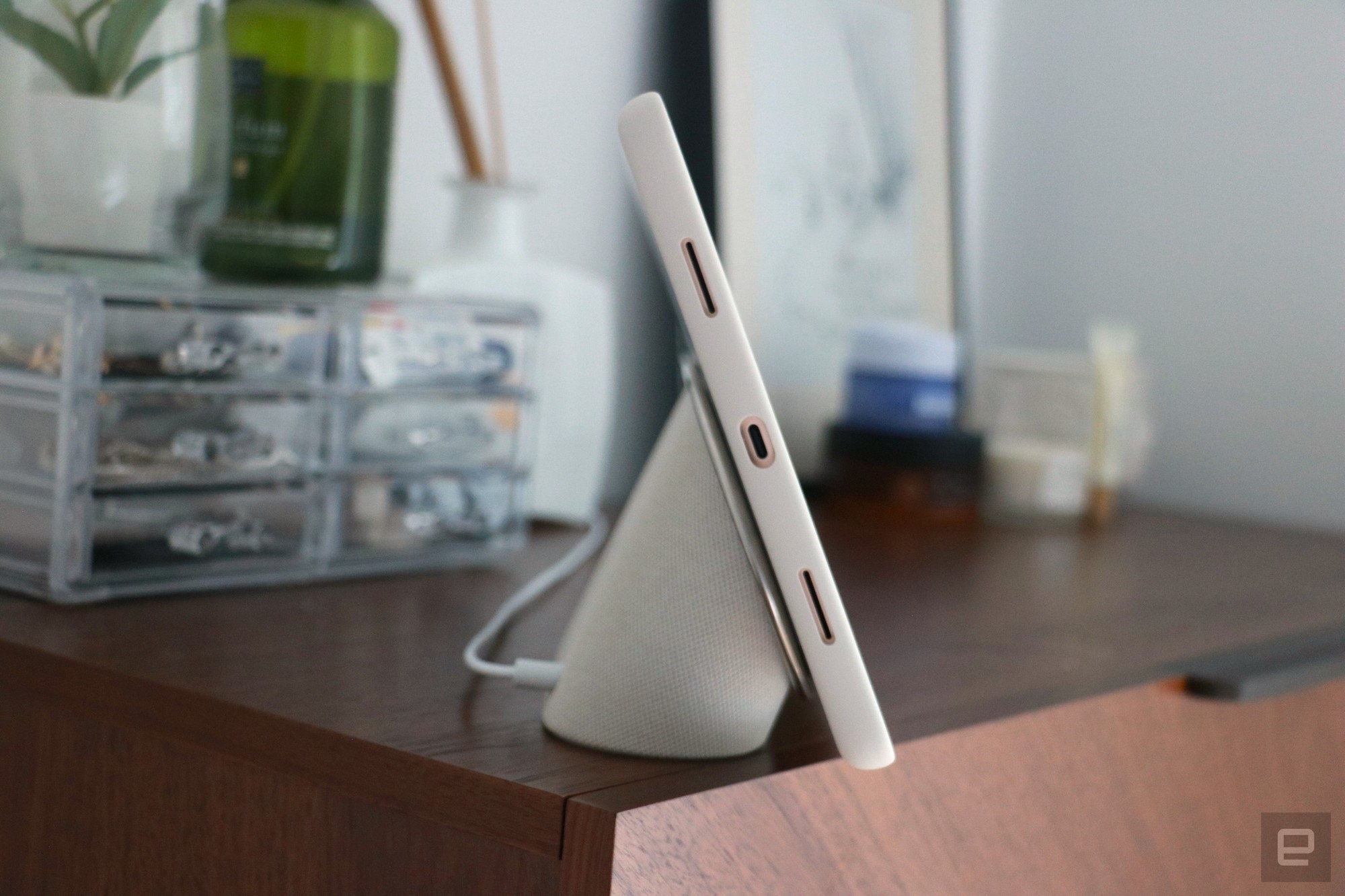 Side view of the Pixel Tablet on a walnut dresser, showing the USB-C port on its left edge. It's docked on the speaker base, with its protective case on. | DeviceDaily.com