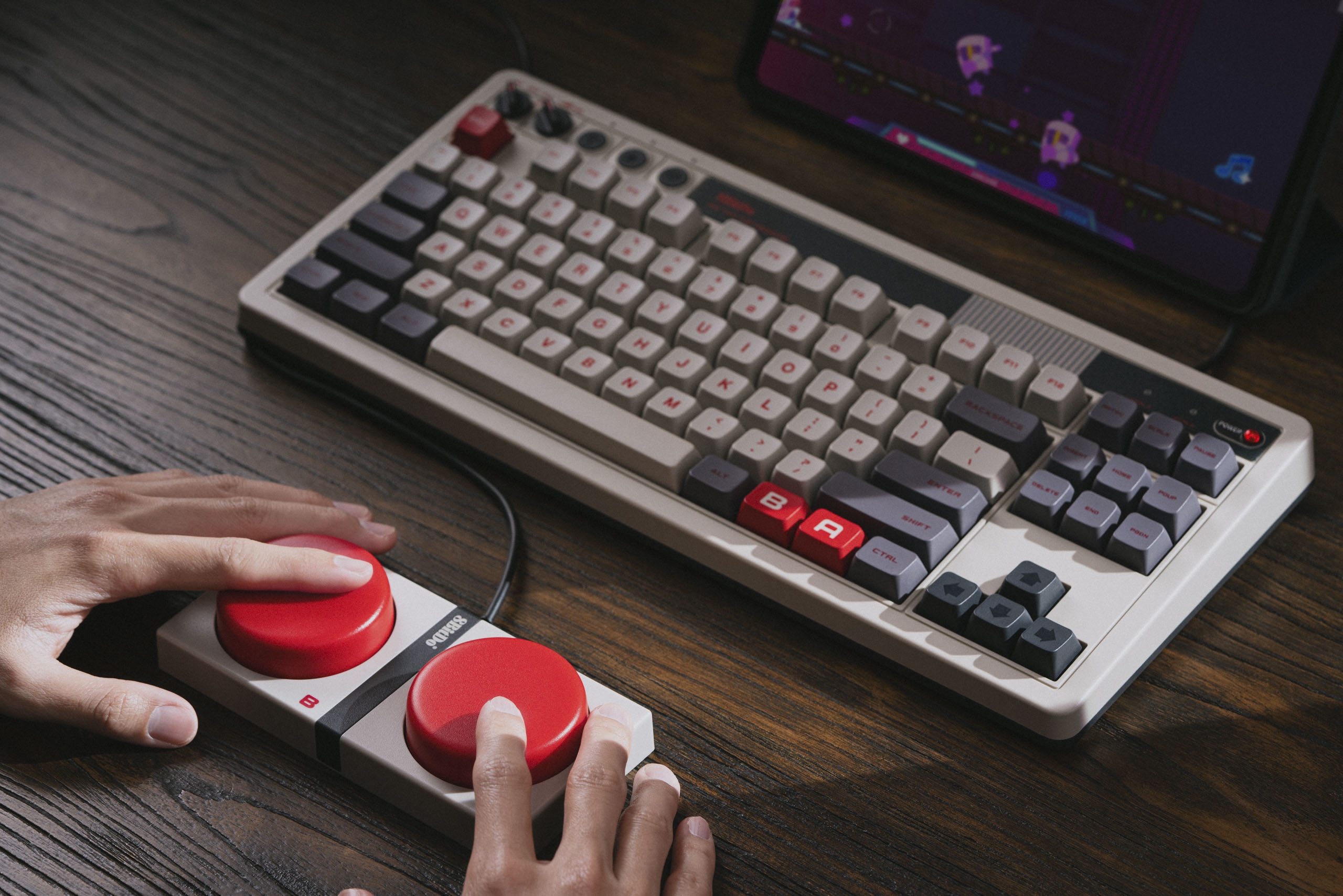 Marketing photography. A NES-colored mechanical keyboard sits on a dark wooden desk. Two hands mash two giant red buttons (also NES-styled) below. | DeviceDaily.com