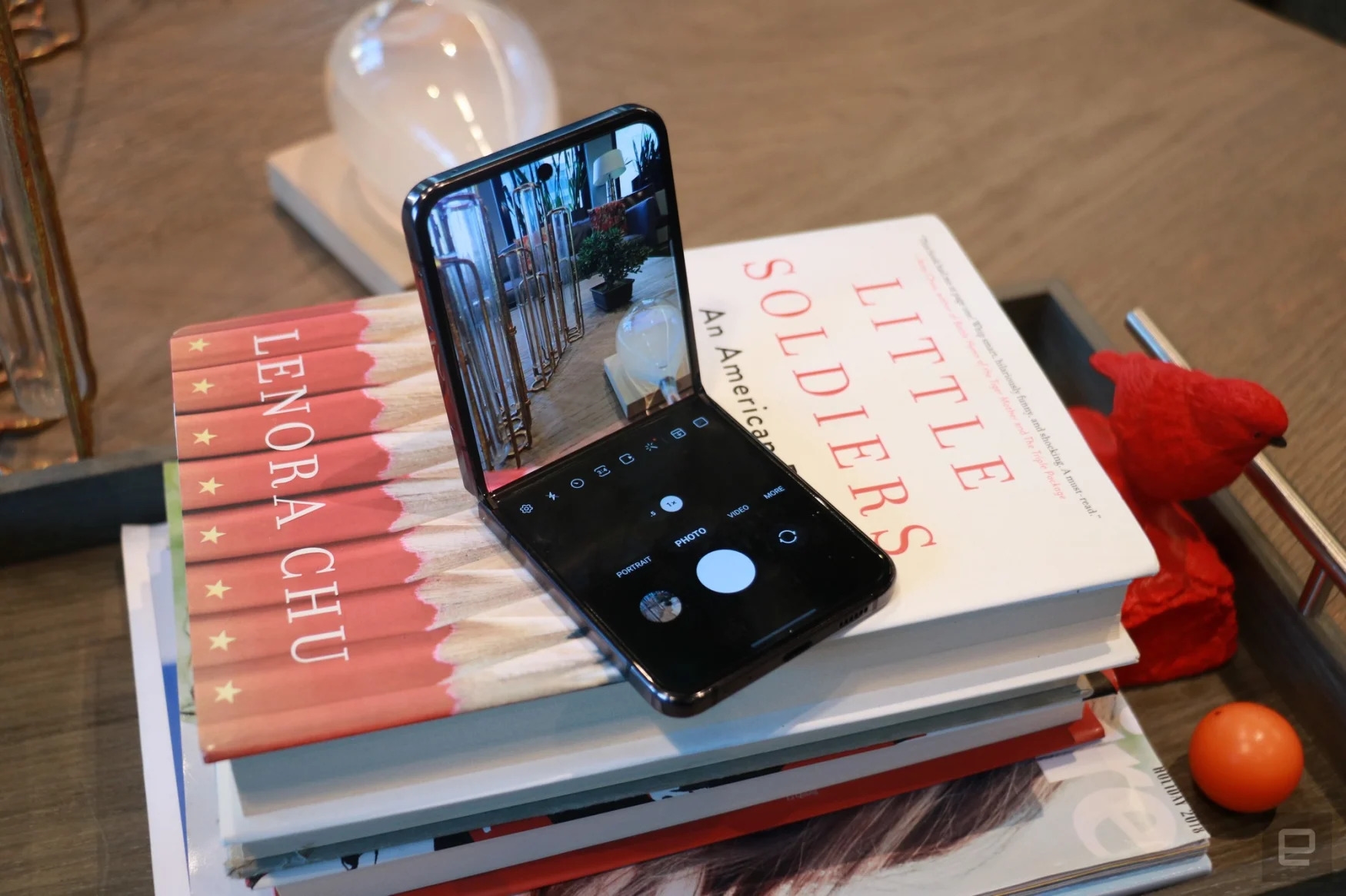 A Samsung Z Flip 5 foldable phone sitting on a pile of books (the top book is | DeviceDaily.com