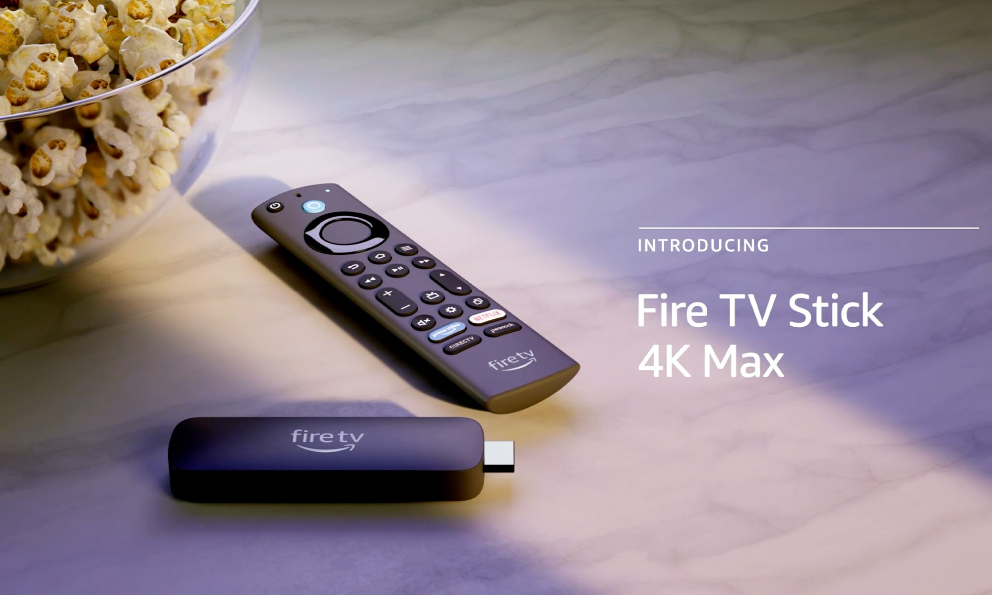 Amazon product photo of the Fire TV Stick 4K Max. The stick-like device sits next to a remote with buttons all over its face. They are on a modern countertop with the edge of a bowl of popcorn visible to the left. | DeviceDaily.com