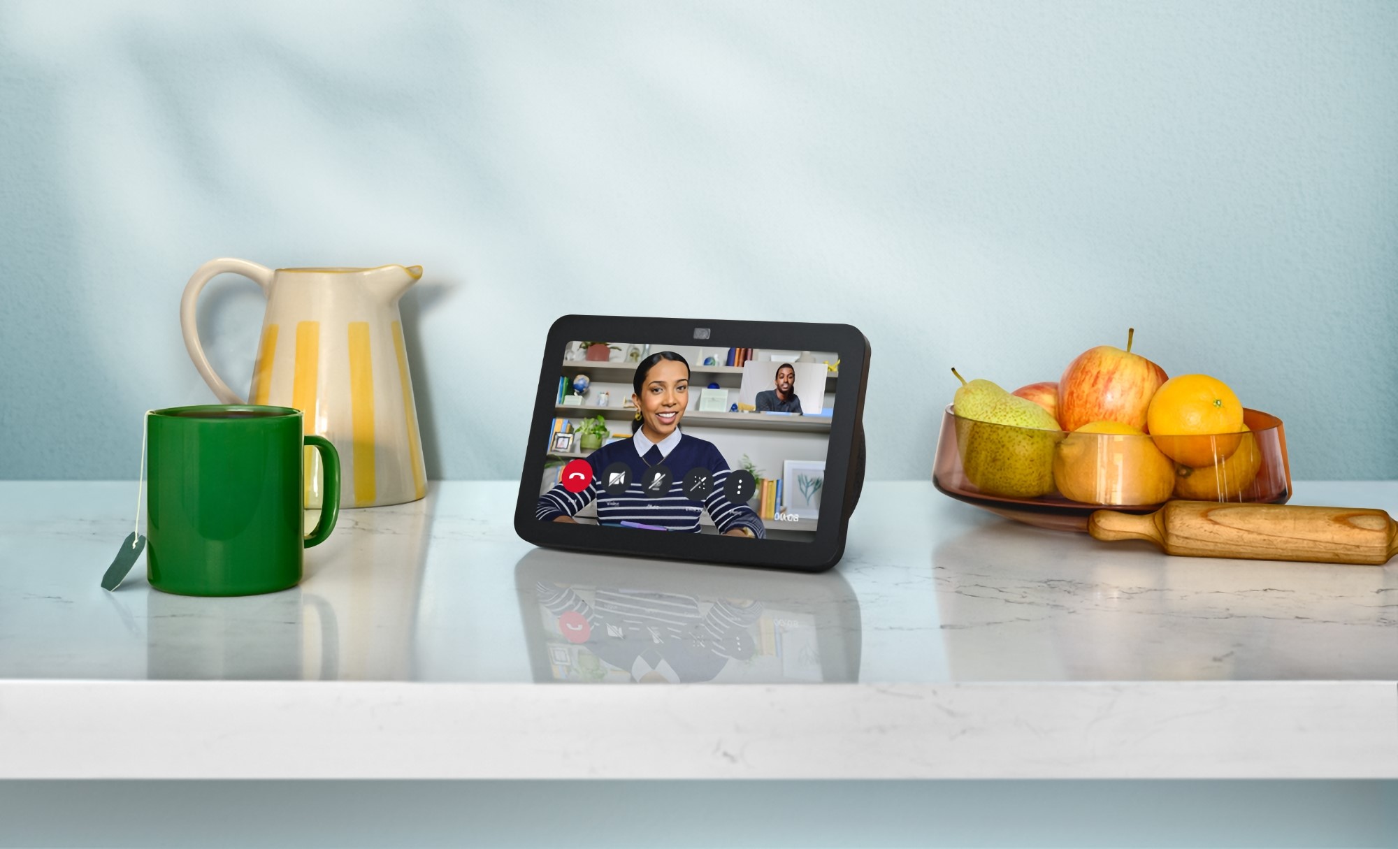 Amazon product photo of an updated Echo Show 8 smart speaker / display. It sits on a luxurious kitchen counter next to a mug, tea pot, and fruit basket. On its screen is a person smiling in a video chat. | DeviceDaily.com