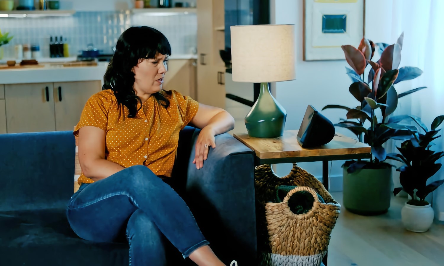 Still from an Amazon promo video. A woman sits on a couch in a posh home, looking at an Echo speaker on her end table with a concerned look on her face. | DeviceDaily.com