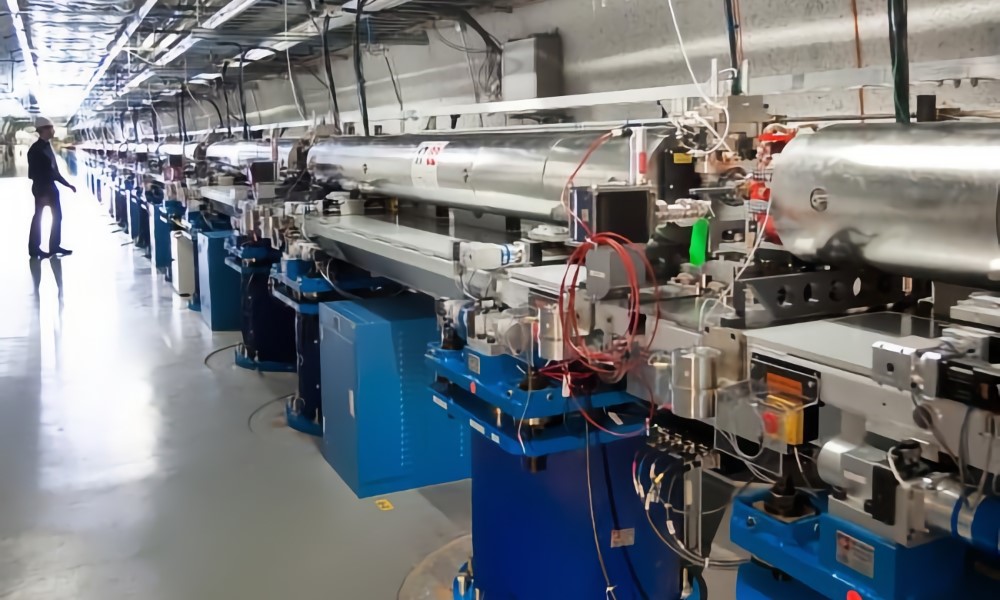 A particle accelerator: a long series of metal tubes and intricate wiring inside an indoor facility. | DeviceDaily.com