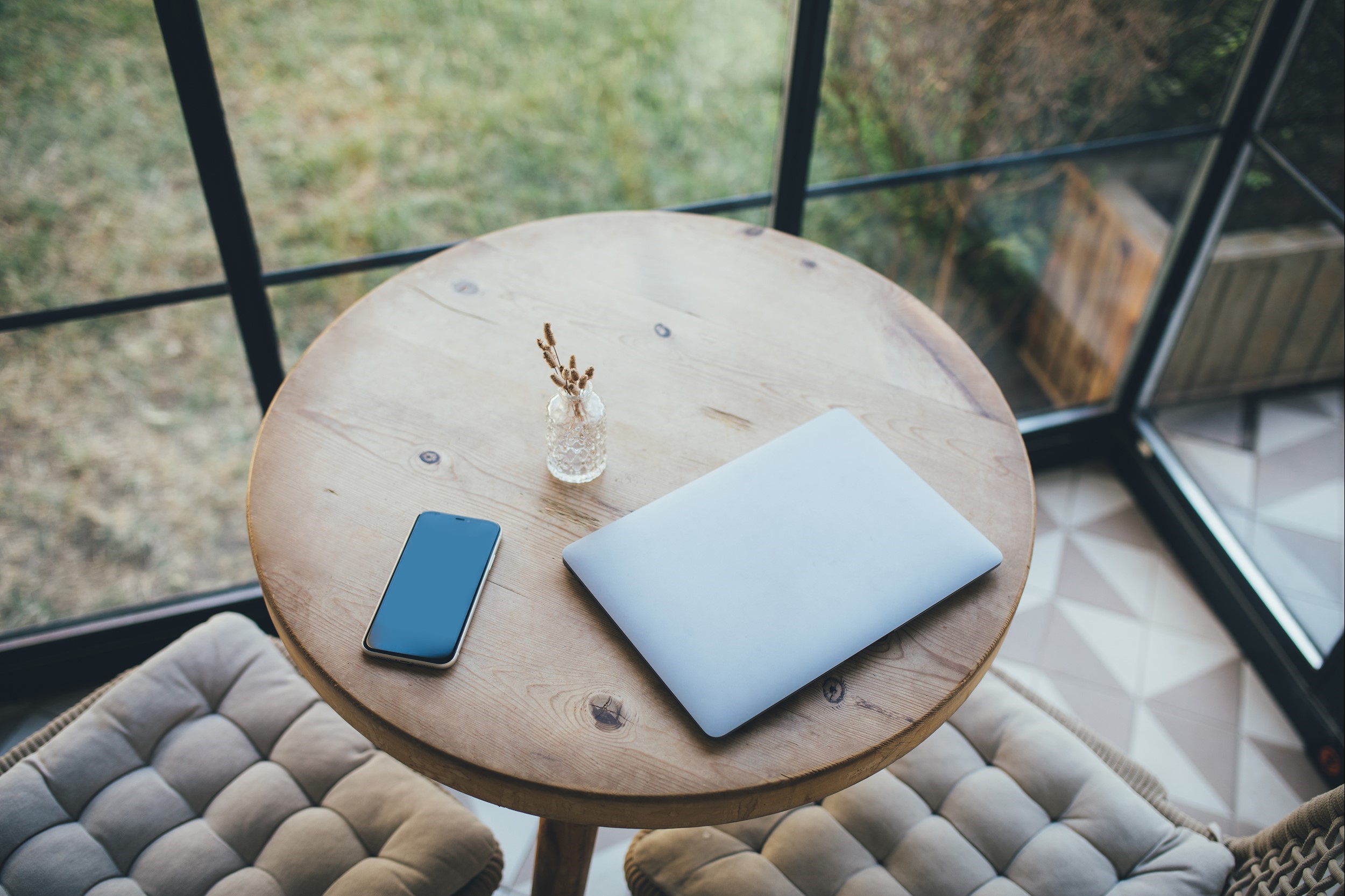 Laptop and smartphone on round wooden table in cozy interior. | DeviceDaily.com